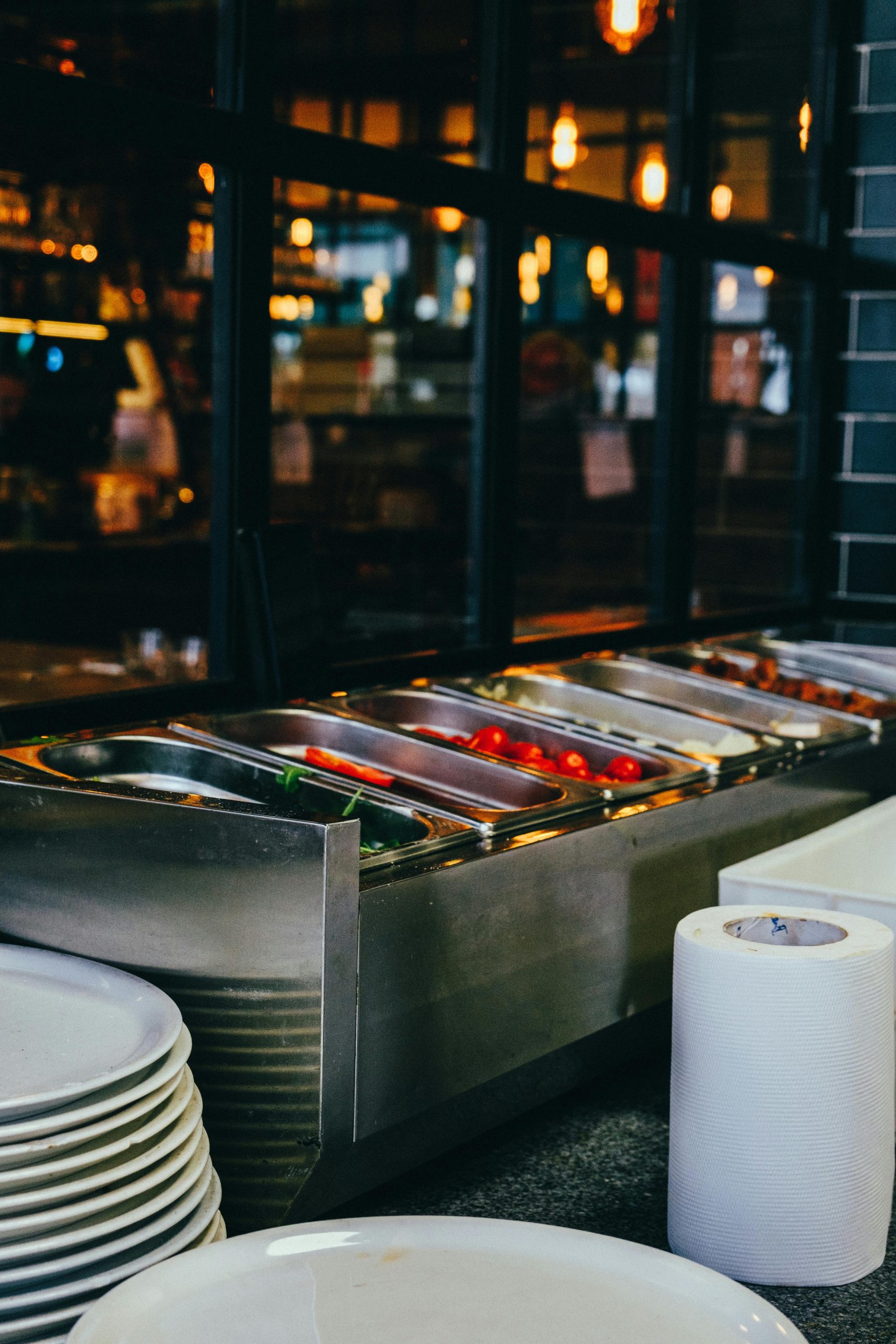A restaurant buffet setup with stainless food containers, plates, and tissue roll